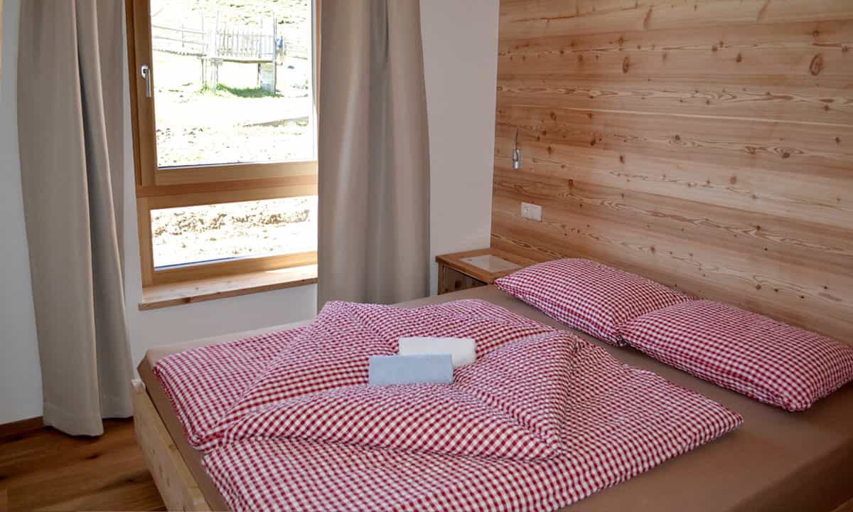 Bedroom with wooden headboard, red gingham bedding, and window view of grassy slope.