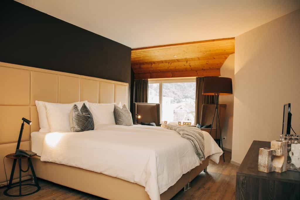 Hotel room with large bed, wood ceiling, and view of buildings and mountains outside window.