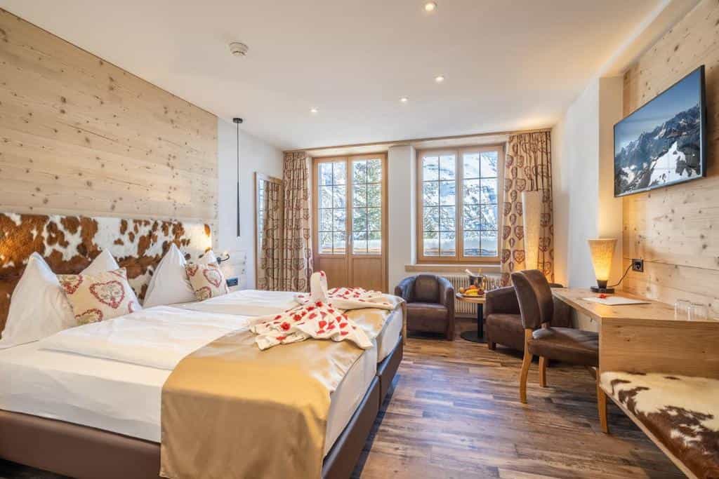 Hotel room with wood paneling, cowhide headboard, and snowy mountain view outside windows.