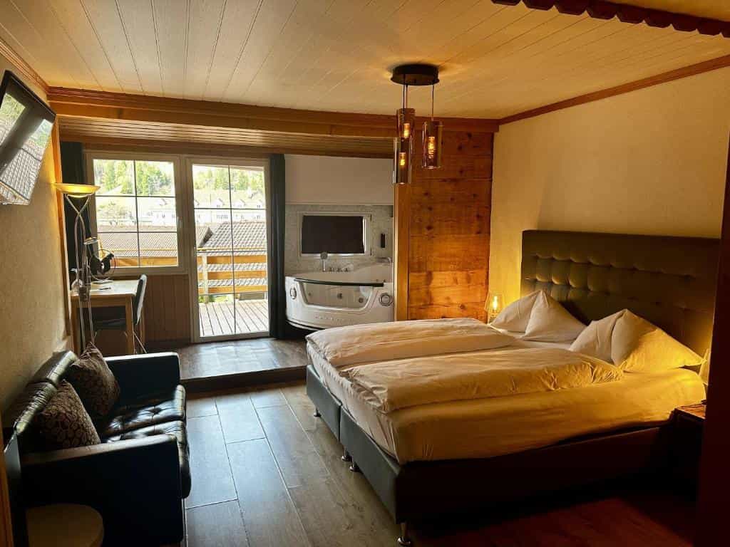 Cozy hotel room with large bed, leather sofa, and indoor jacuzzi near balcony access.