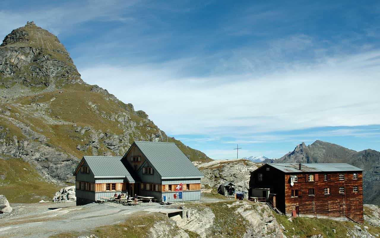 Cabane de Prafleuri mountain huts with hikers near rocky peaks under a blue sky.