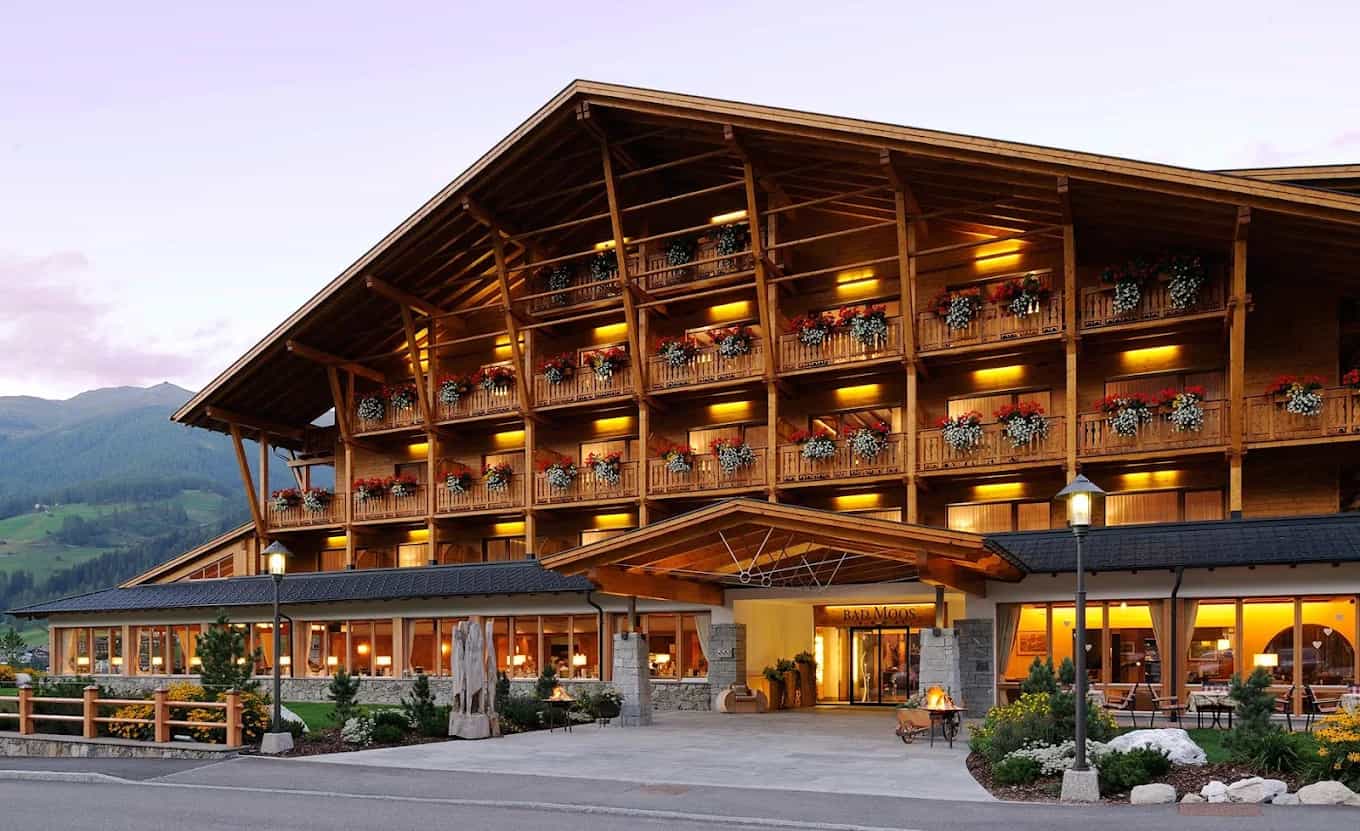 Bad Moos Dolomites Spa Resort exterior with wooden balconies and warm interior lighting in the Alps