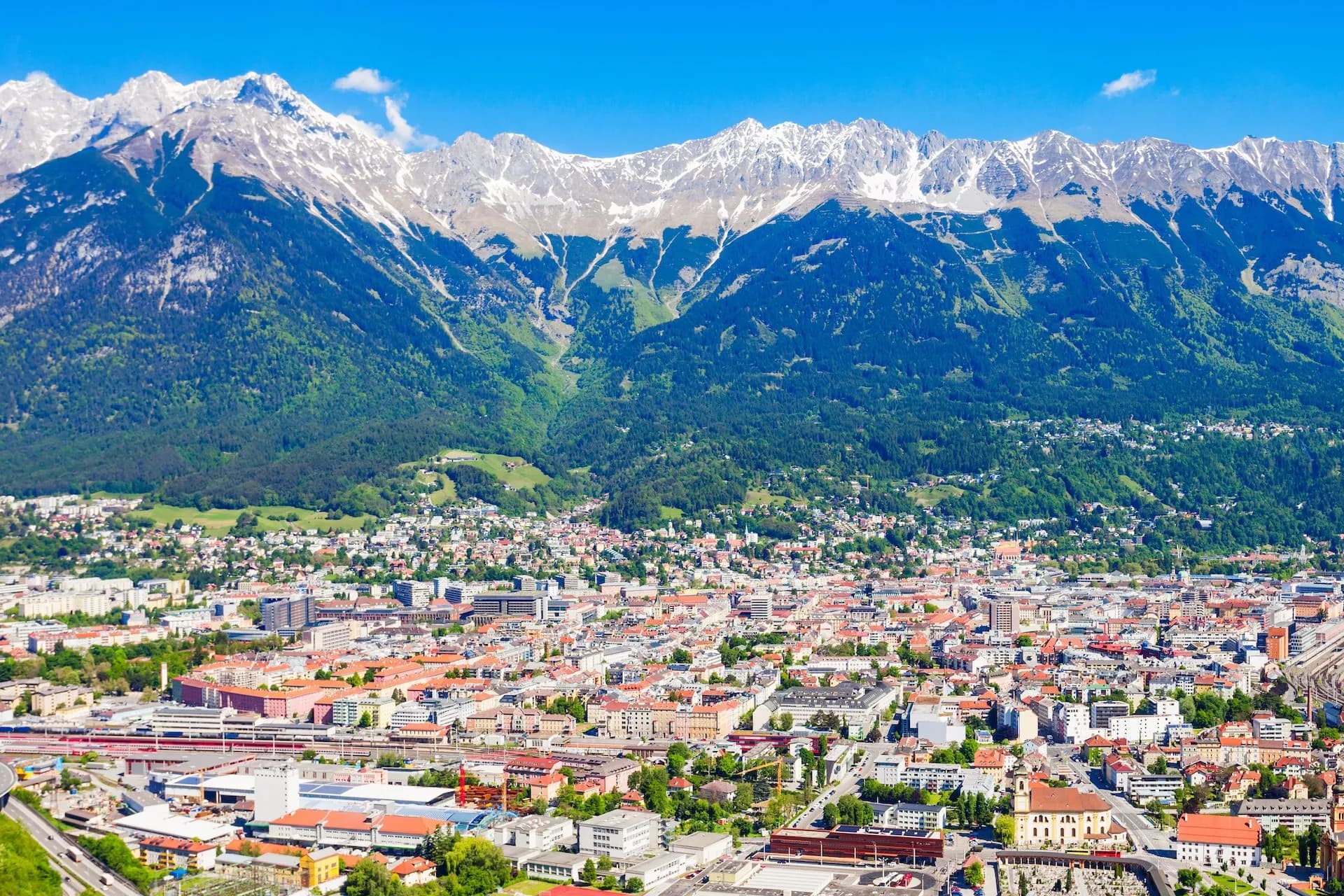 City of Innsbruck nestled below snow-capped Alpine mountains under a clear blue sky.