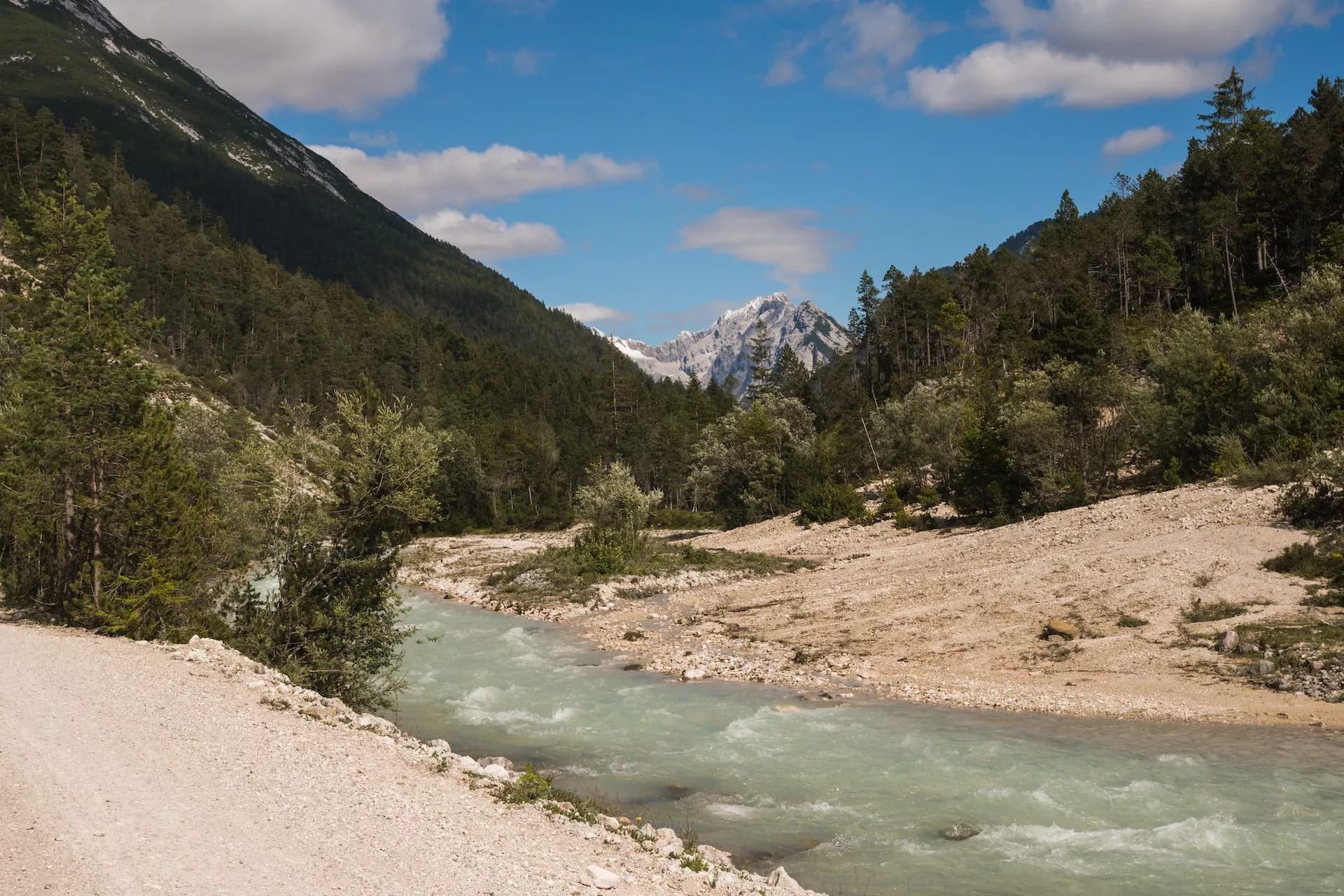 Mountain river with turquoise water flowing through a valley with forested slopes and distant snowy peaks.