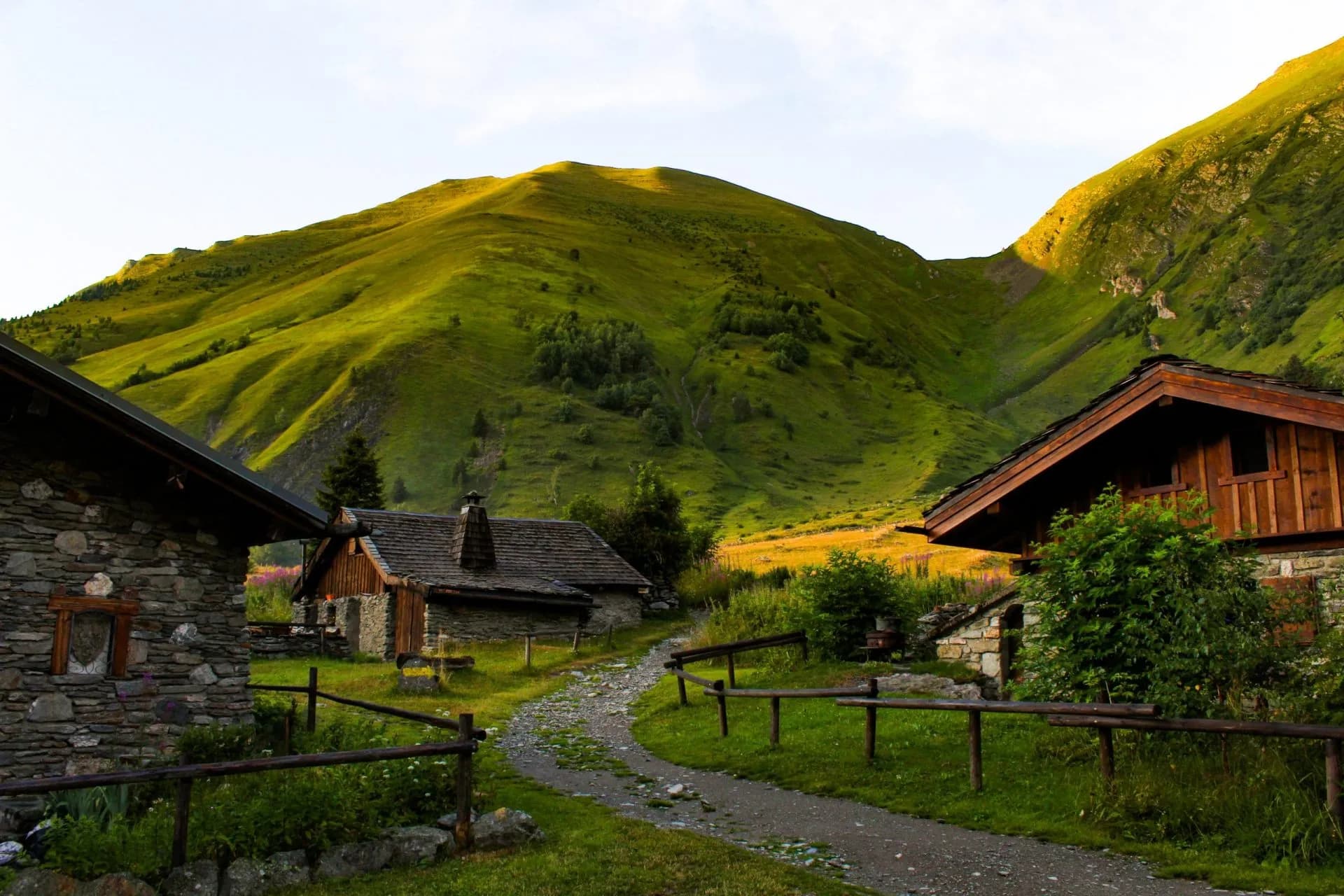 Stone and wood alpine chalets nestled in a valley below steep, grassy mountainsides