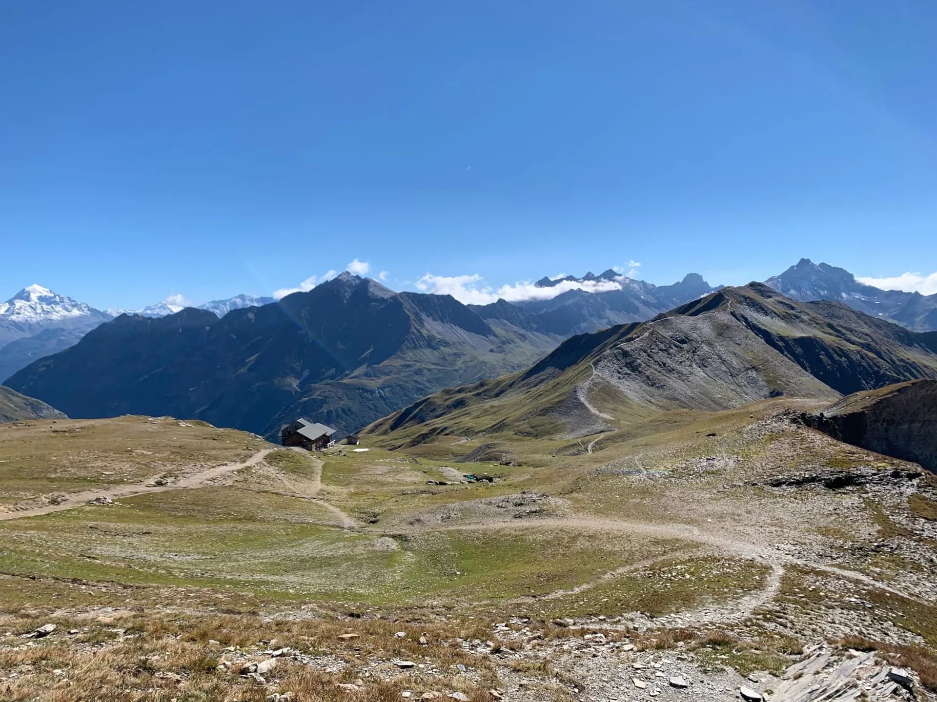Mountain refuge, Refuge de la Croix du Bonhomme, nestled in grassy alpine terrain under a clear blue sky.
