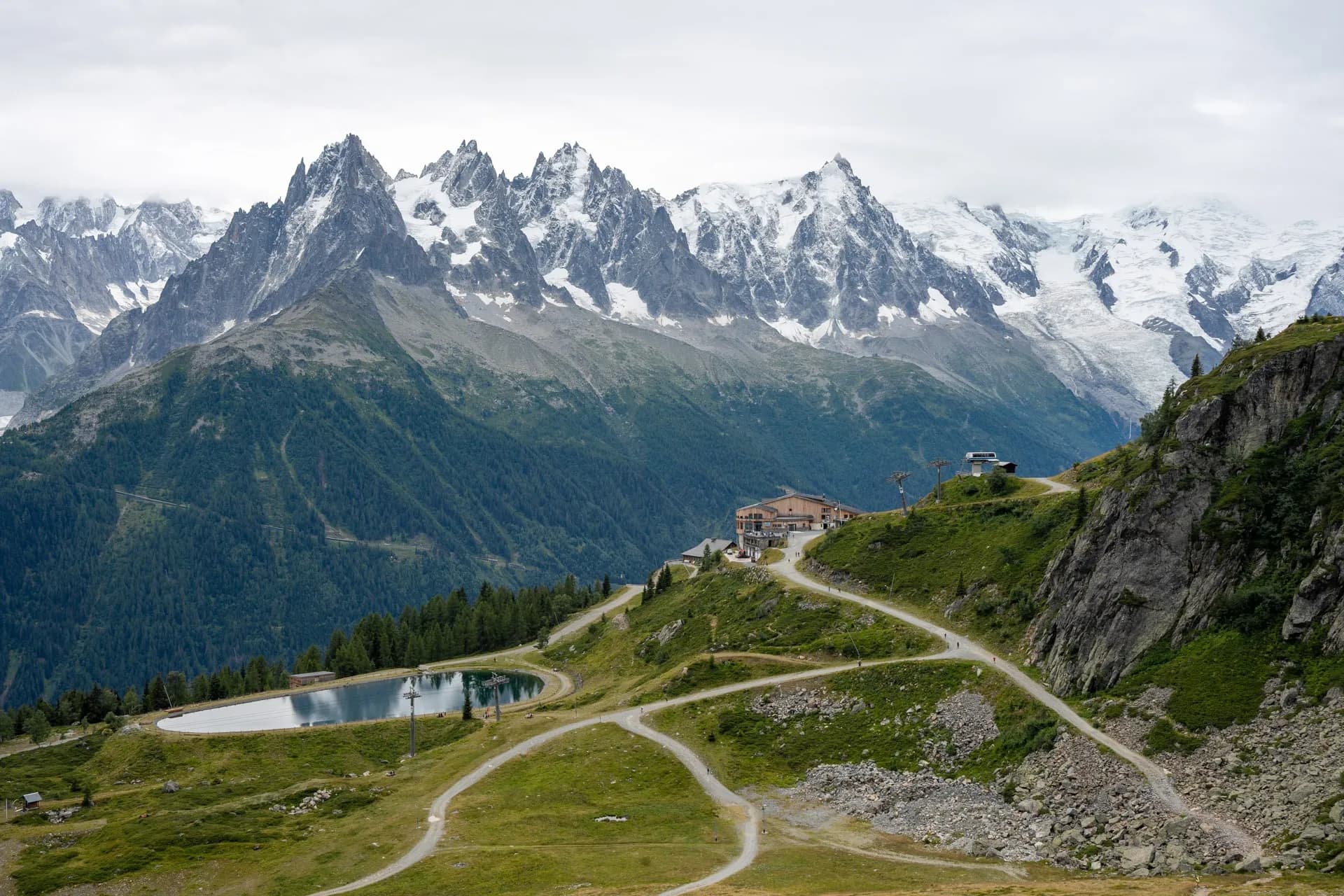 Mountain resort with reservoir and winding paths below snow-capped alpine peaks, La Flegere.