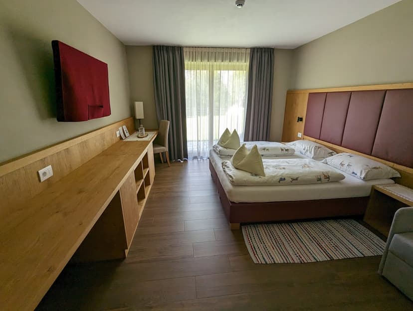 Hotel room with double bed, long wooden desk, and balcony doors at Rifugio Fanes.