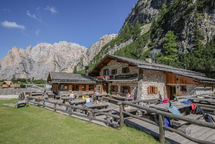 Rifugio Scotoni stone hut with outdoor dining area against dramatic mountain backdrop.