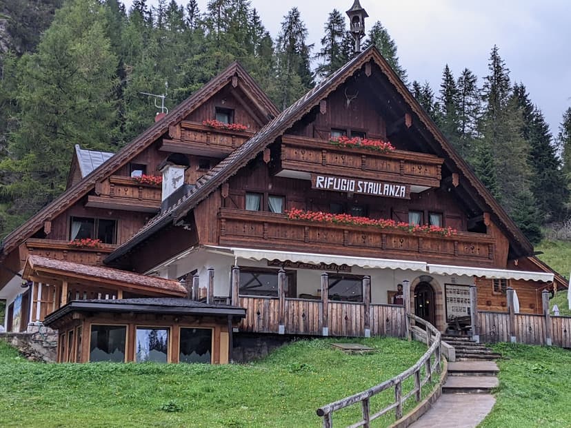 Rifugio Staulanza wooden mountain lodge with flower boxes against a dense pine forest.