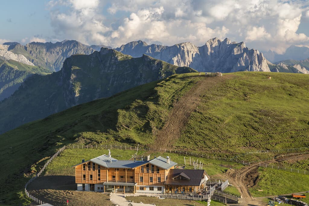 Rifugio Sasso Piatto wooden lodge nestled on grassy alpine slope below jagged mountains.