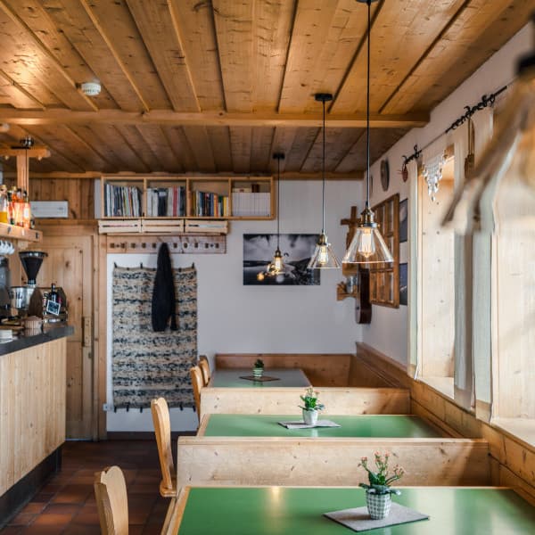 Interior of Franz Kostner Hut with wooden paneling, green tables, and hanging pendant lights.
