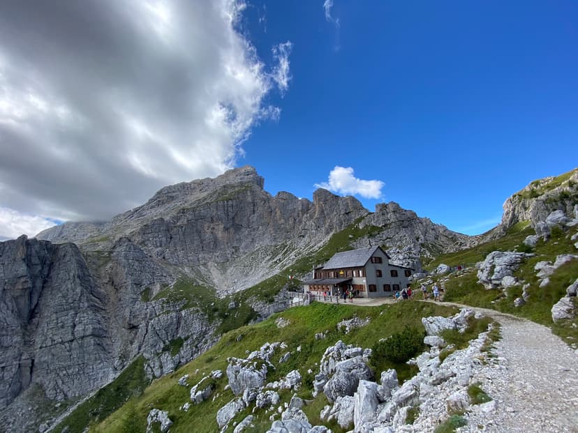 Rifugio Adolfo Sonino al Coldai mountain hut with hikers on a trail below rocky peaks.