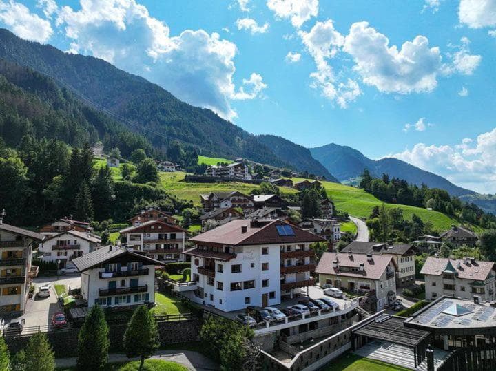 Alpine village with traditional houses nestled on a green mountain slope under a blue sky.