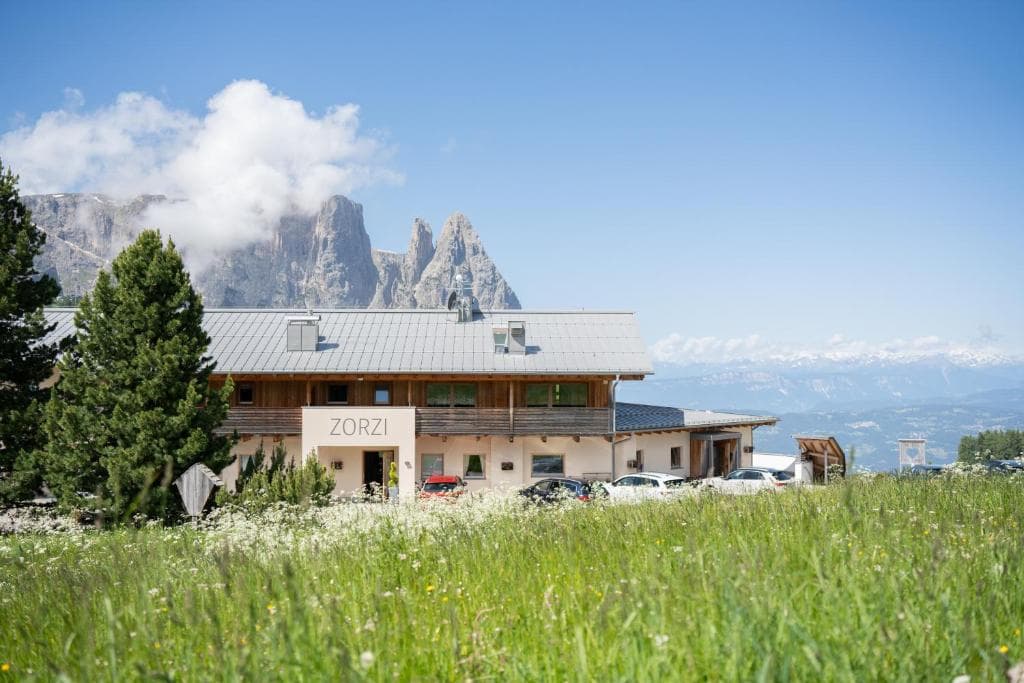 Mountain lodge named Zorzi in a grassy alpine meadow with rocky peaks in the background.