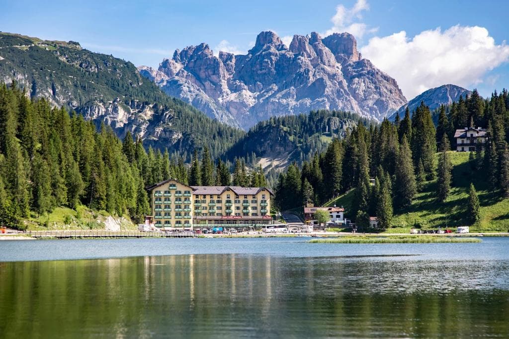 Hotel on the shore of an alpine lake surrounded by pine forests and jagged mountain peaks.