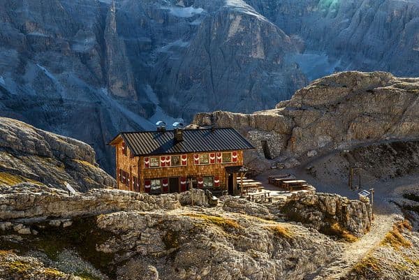Wooden mountain hut with outdoor seating nestled in a rocky Alpine landscape.