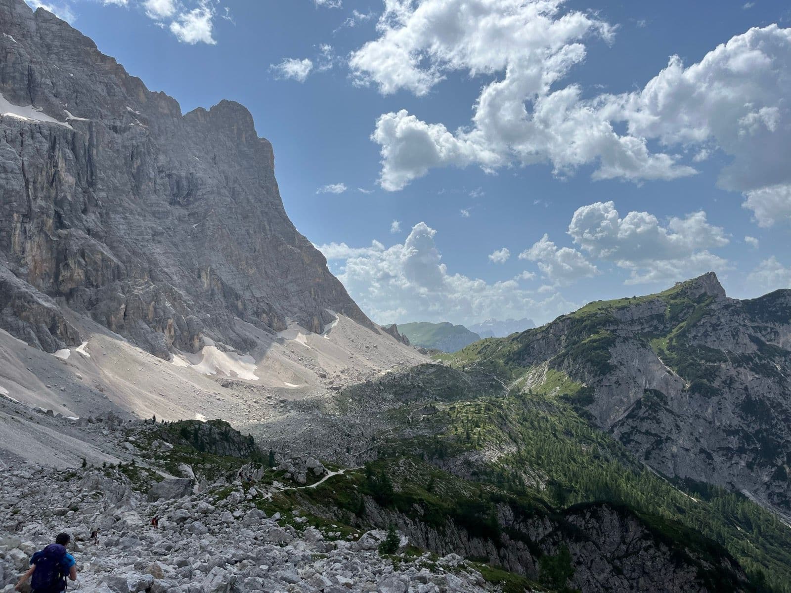 Hikers on a rocky mountain trail in the Southern Alps under a blue sky with clouds.