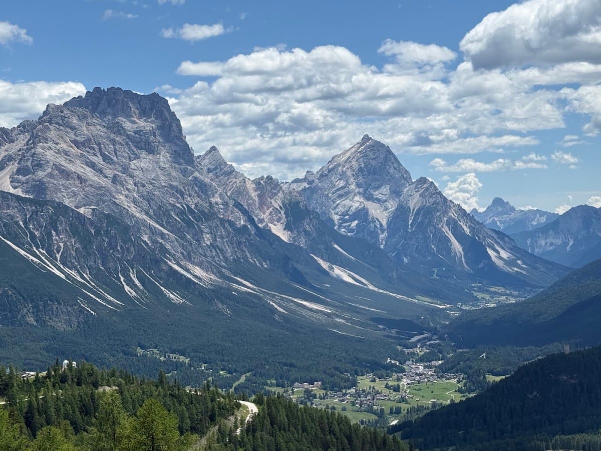 Alpine mountain valley with rocky peaks, pine forest, and scattered clouds