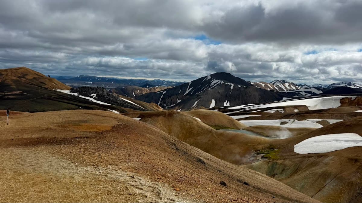 Barren mountain landscape with snow patches under cloudy sky