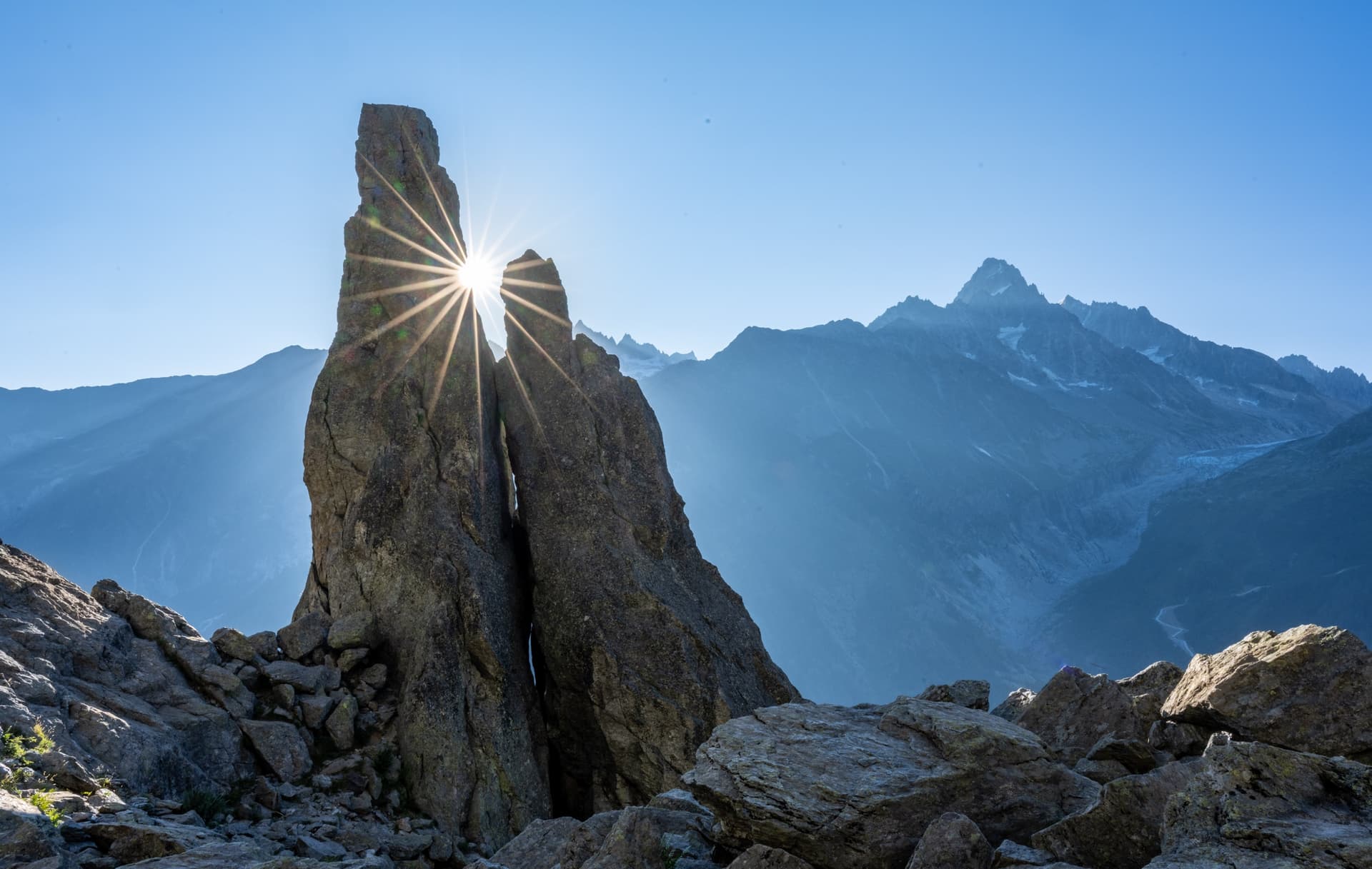 Sunburst shining through a tall rock spire with mountain peaks in the background