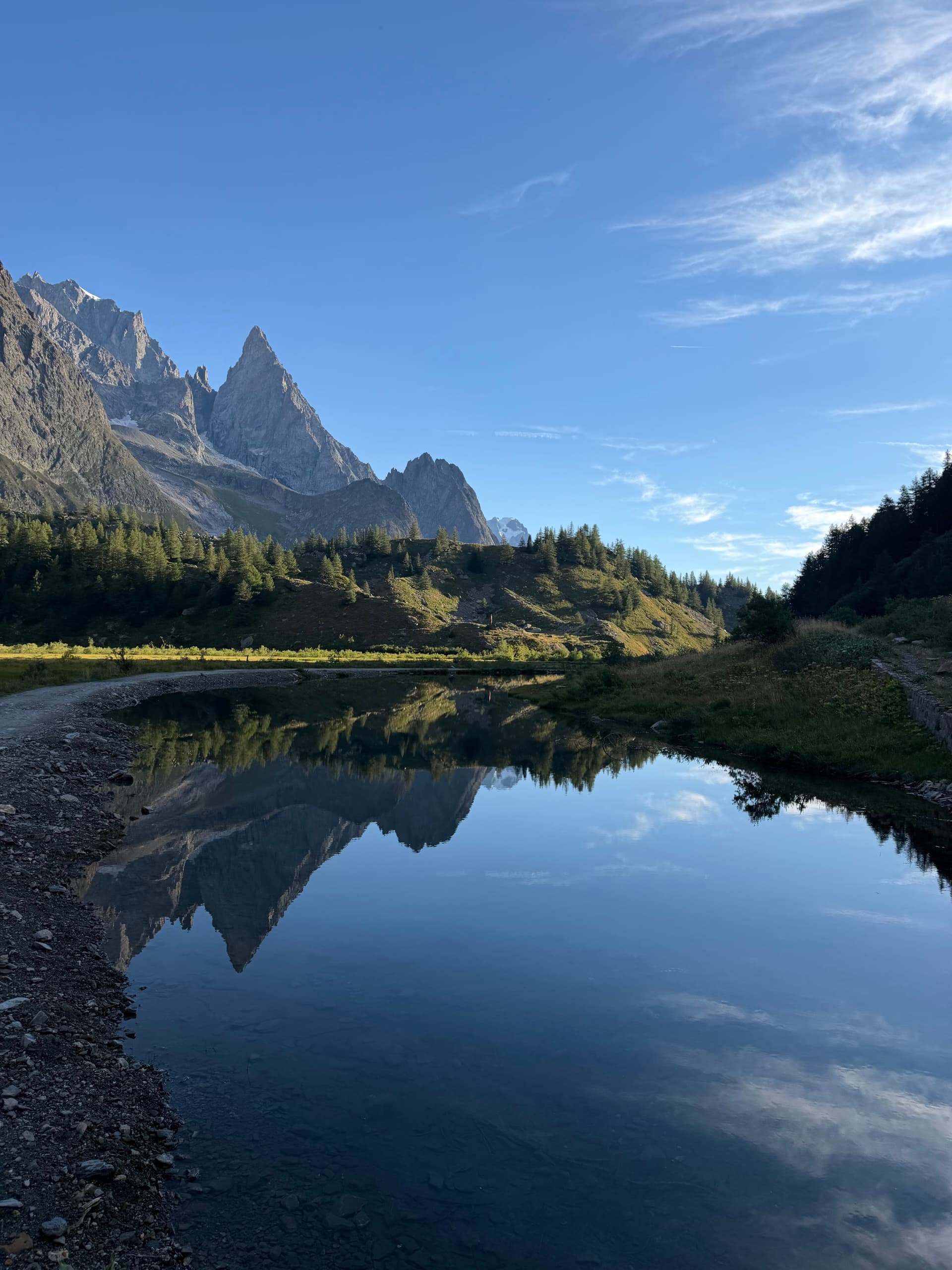 Alpine lake reflecting jagged granite peaks and pine trees under a blue sky