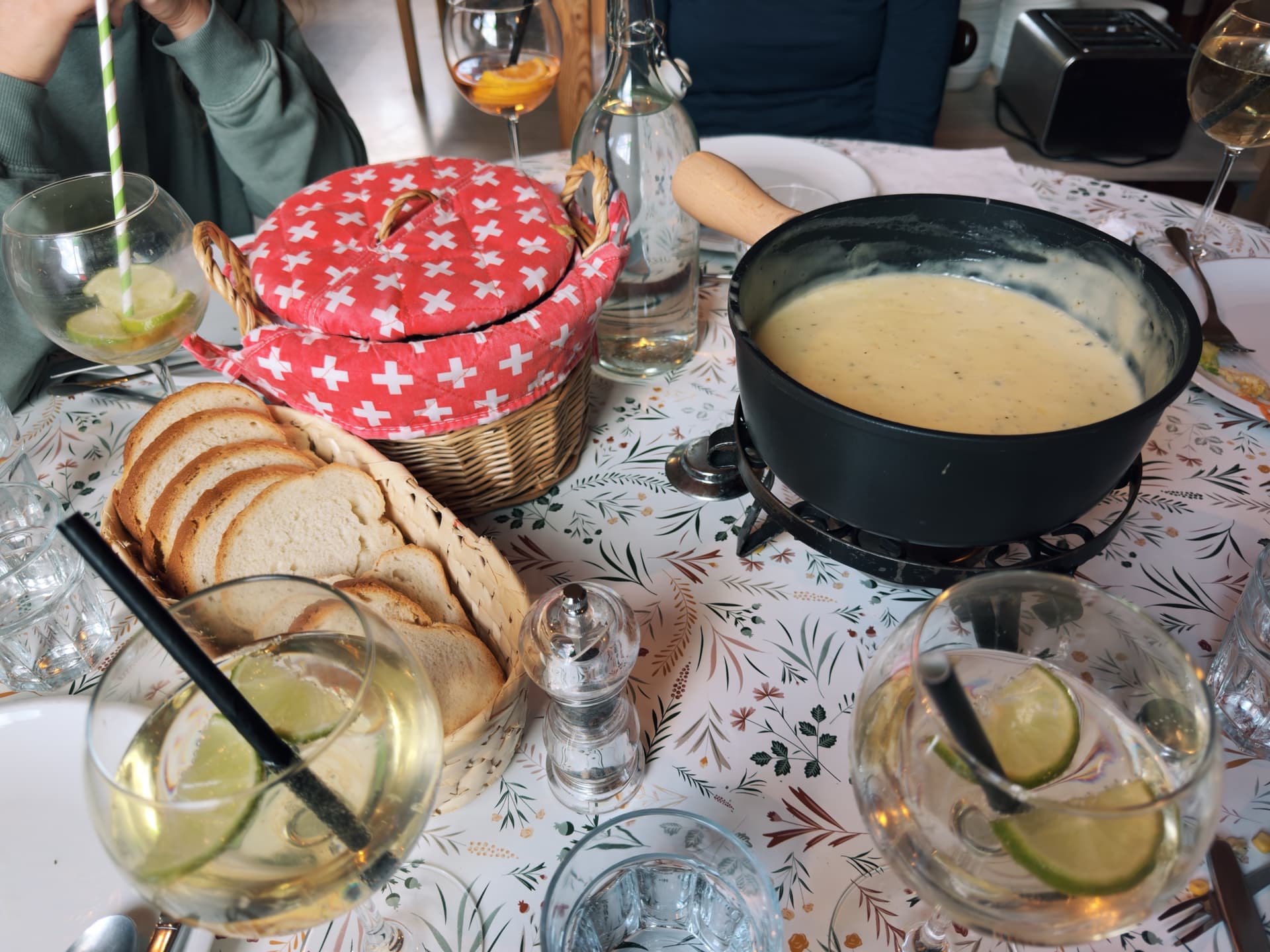 Fondue pot of melted cheese served with sliced bread and drinks on restaurant table