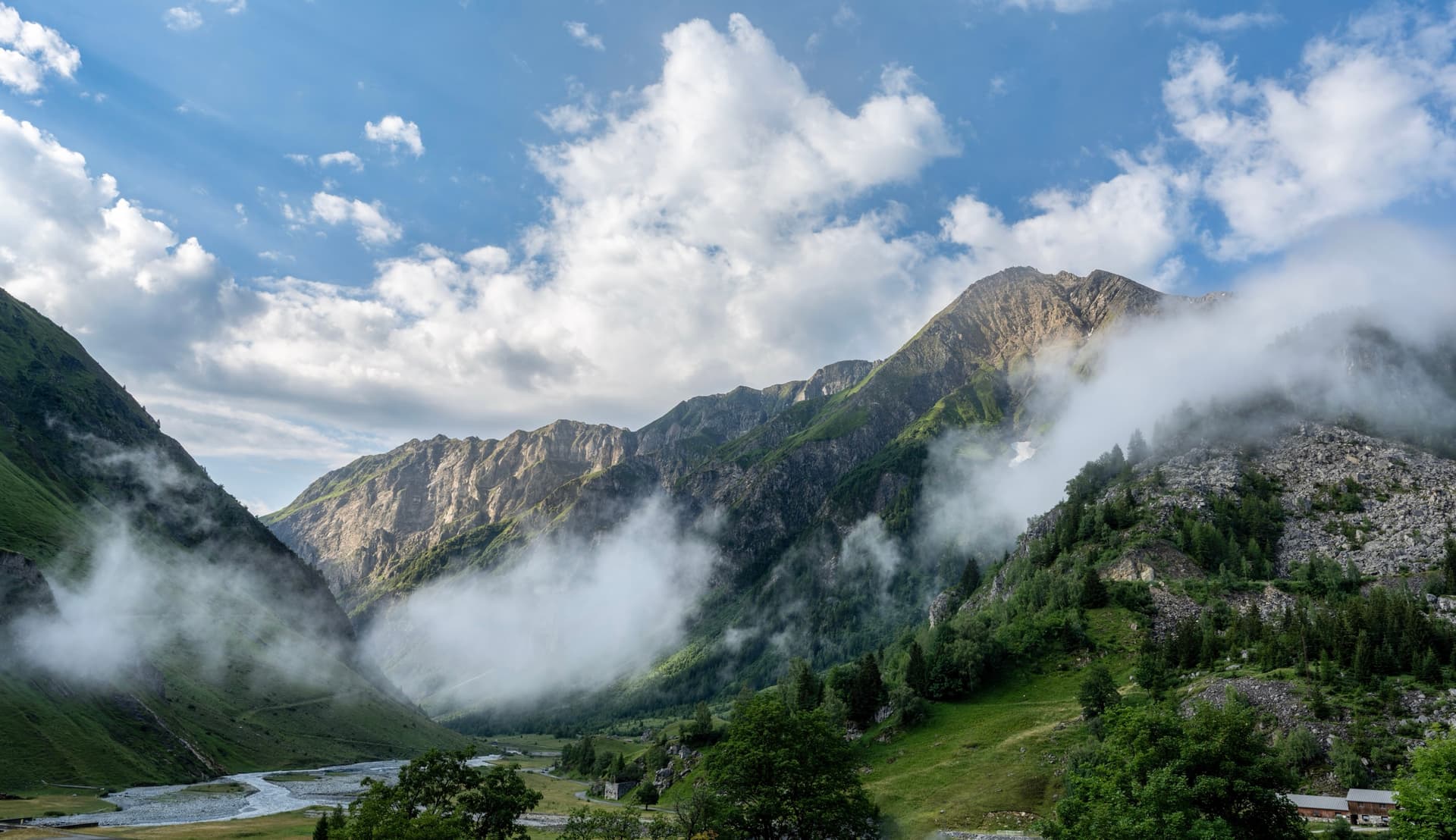 Clouds rising from a green mountain valley with a winding river below