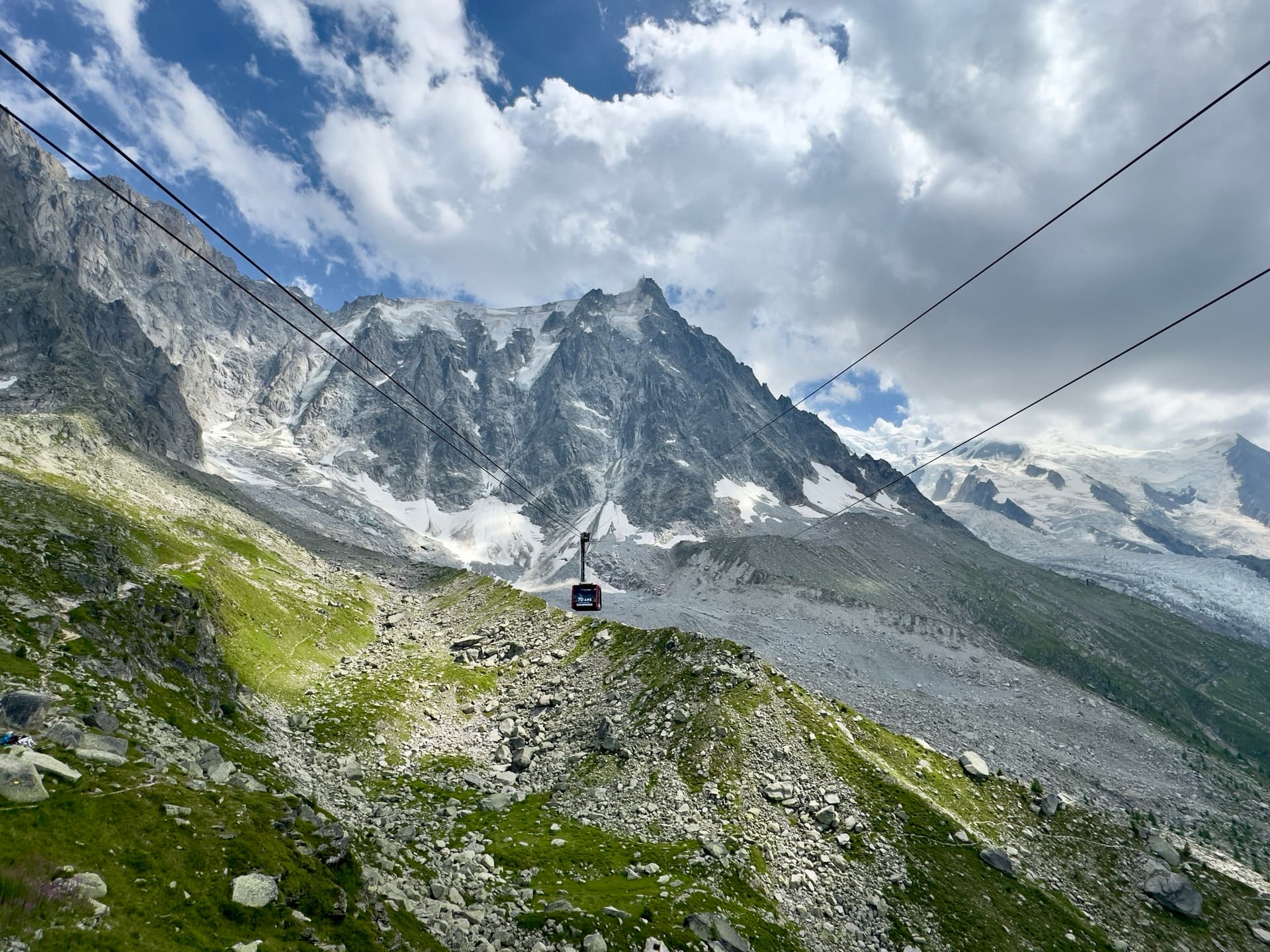 Cable car suspended on cables over a rocky glacier valley with snow-capped mountain peaks