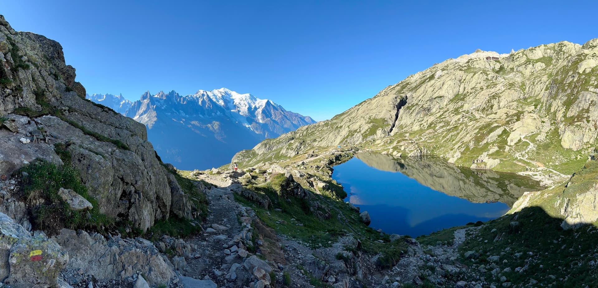 Alpine lake in a rocky mountain basin with hiking trail under blue sky