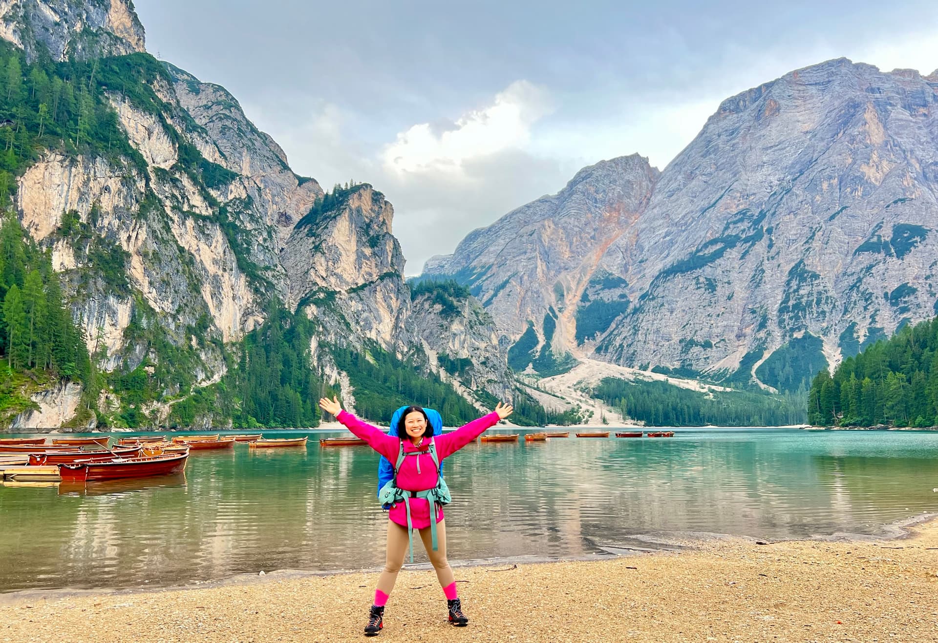 Hiker celebrating with arms raised by alpine lake and mountain peaks