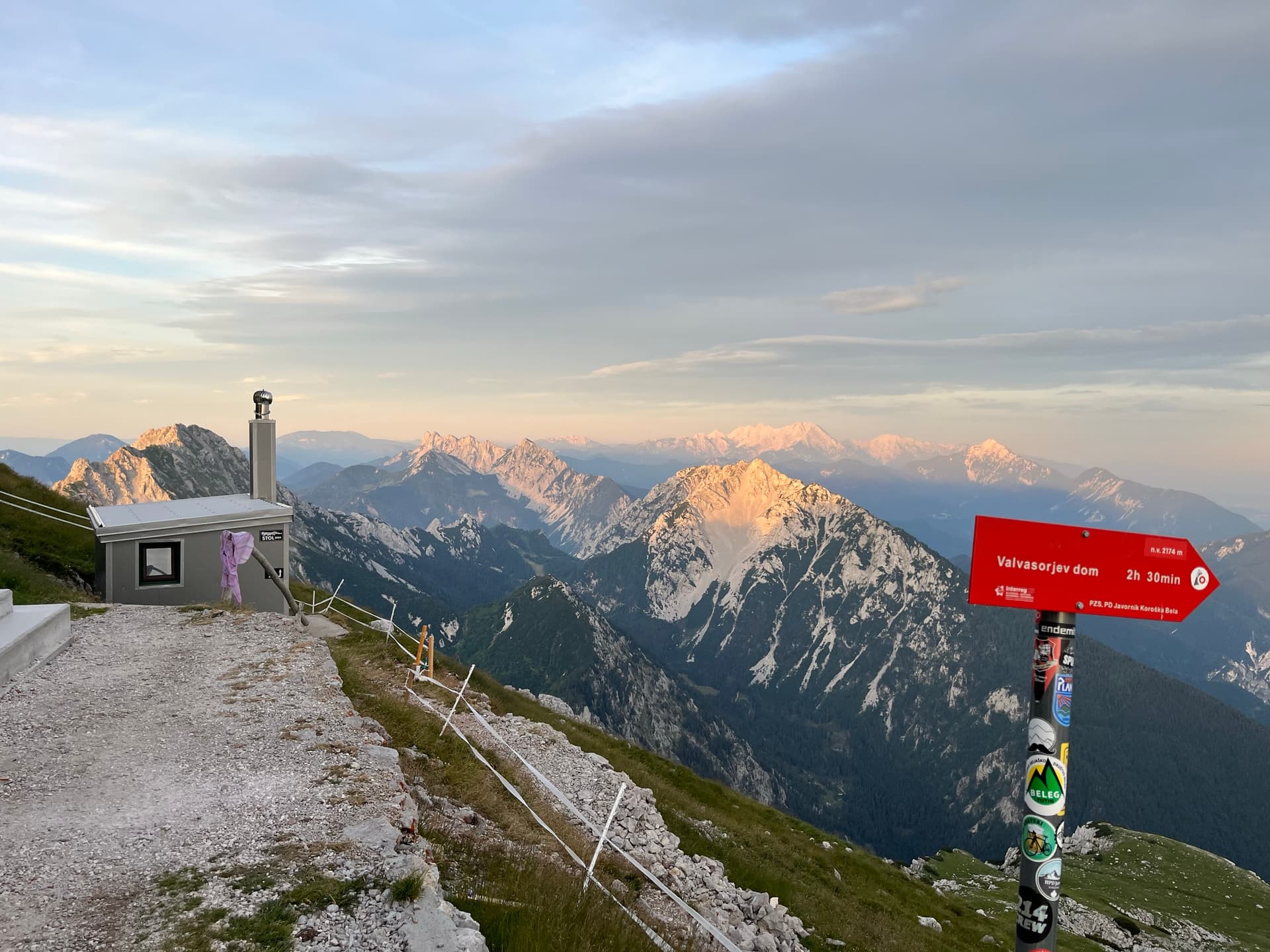 Mountain hut and hiking sign overlooking alpine peaks at dawn