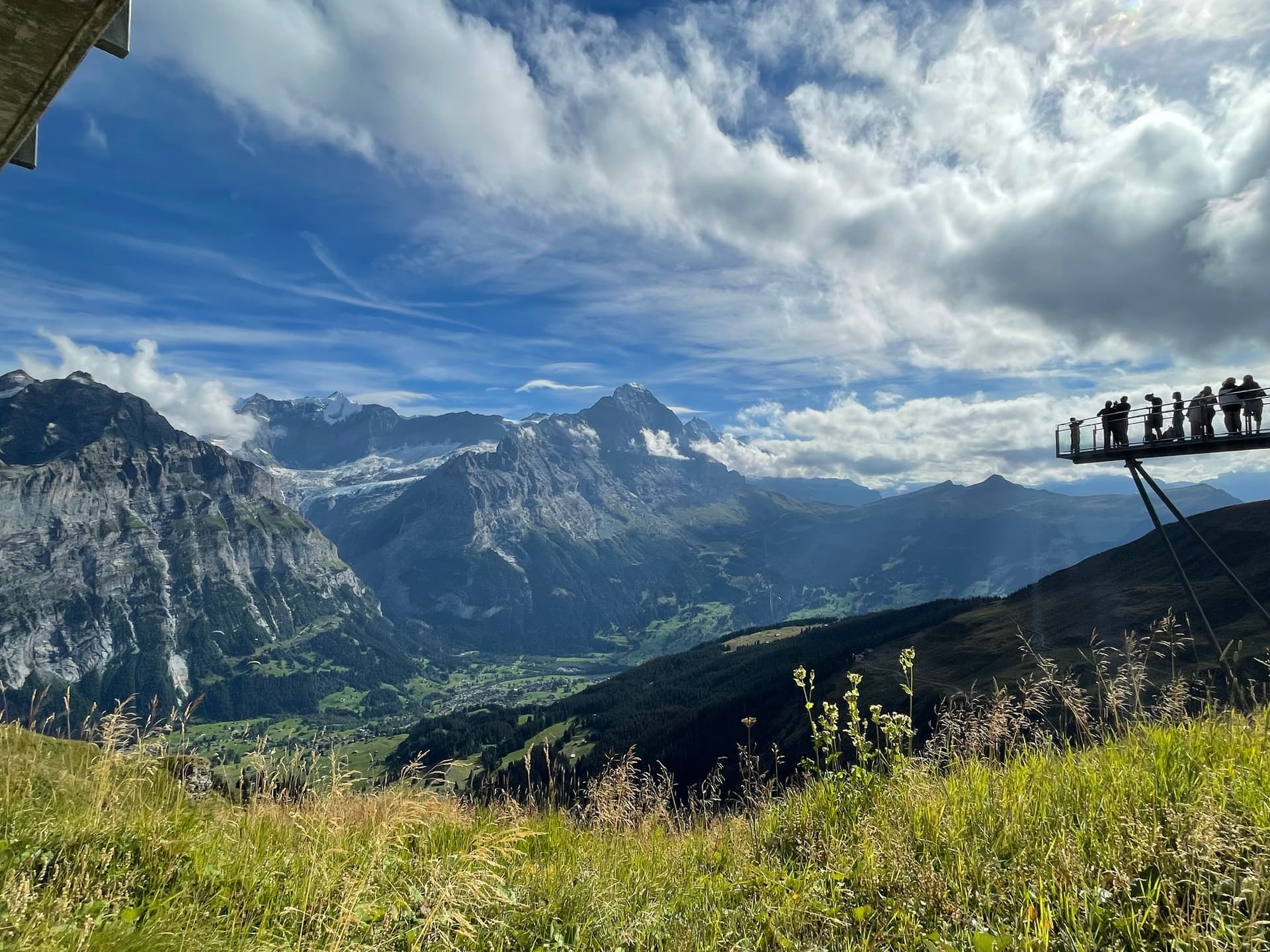 Viewing platform with people overlooking an alpine valley and snow-capped mountain peaks