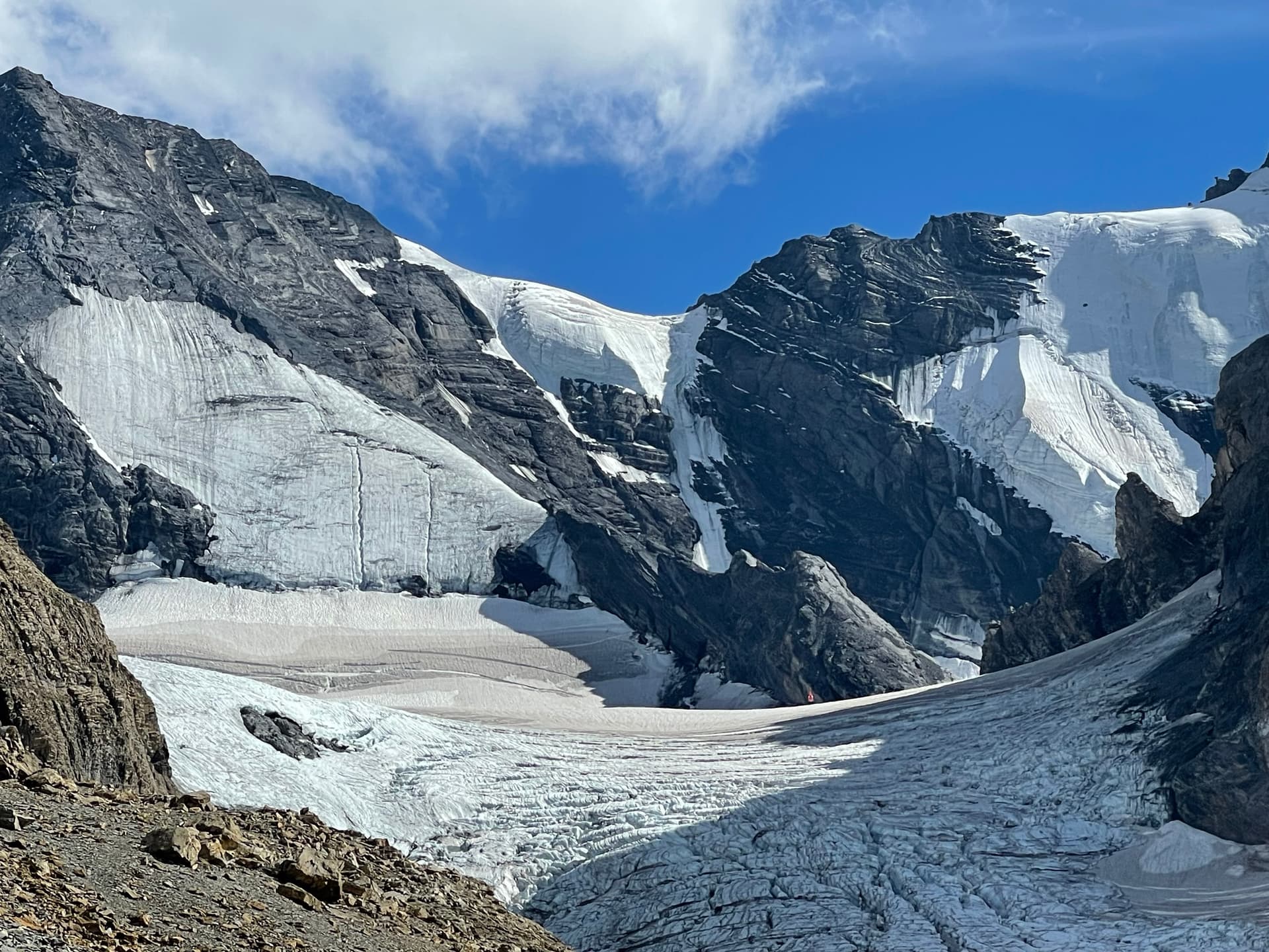 Glacier nestled between rugged rocky mountain peaks under a blue sky