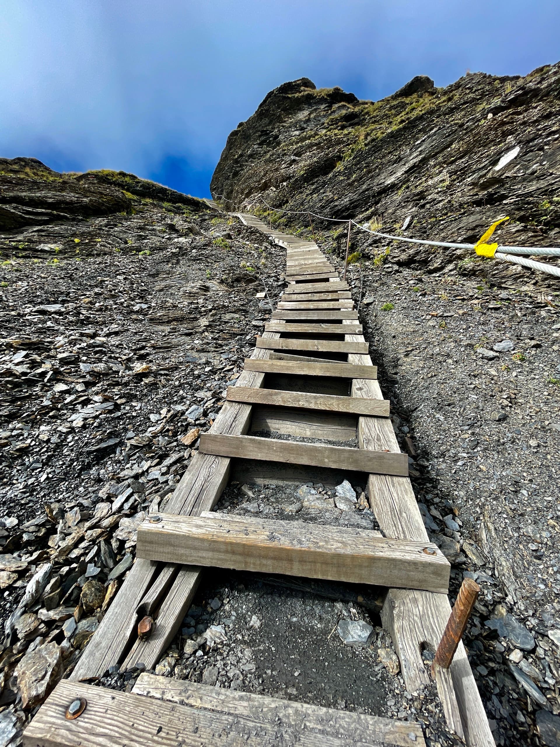 Wooden steps going up a steep scree slope with a safety cable