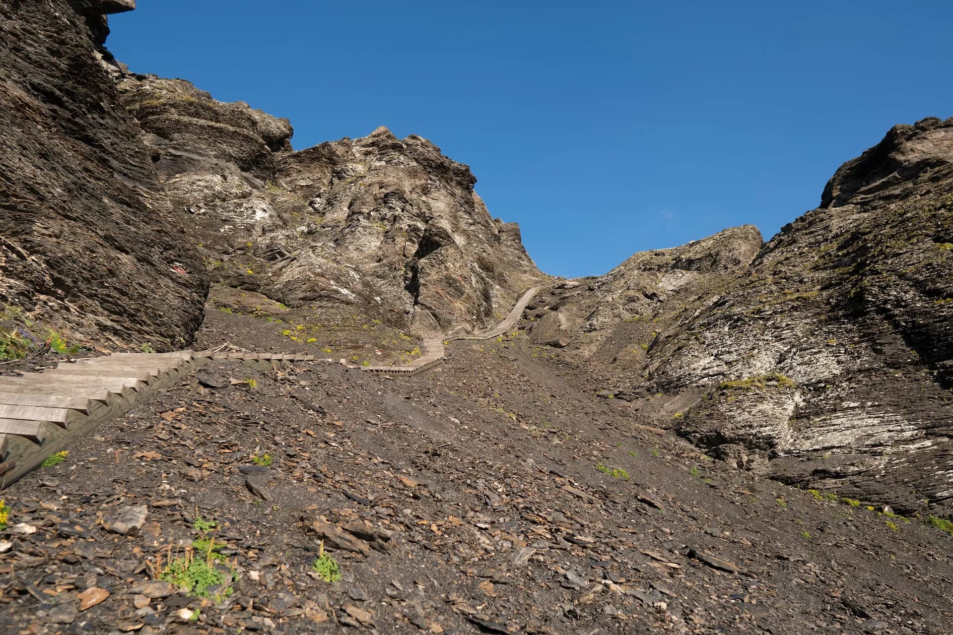 Wooden stairs ascending steep, rocky slope toward Sefinenfurgge Pass under clear blue sky.