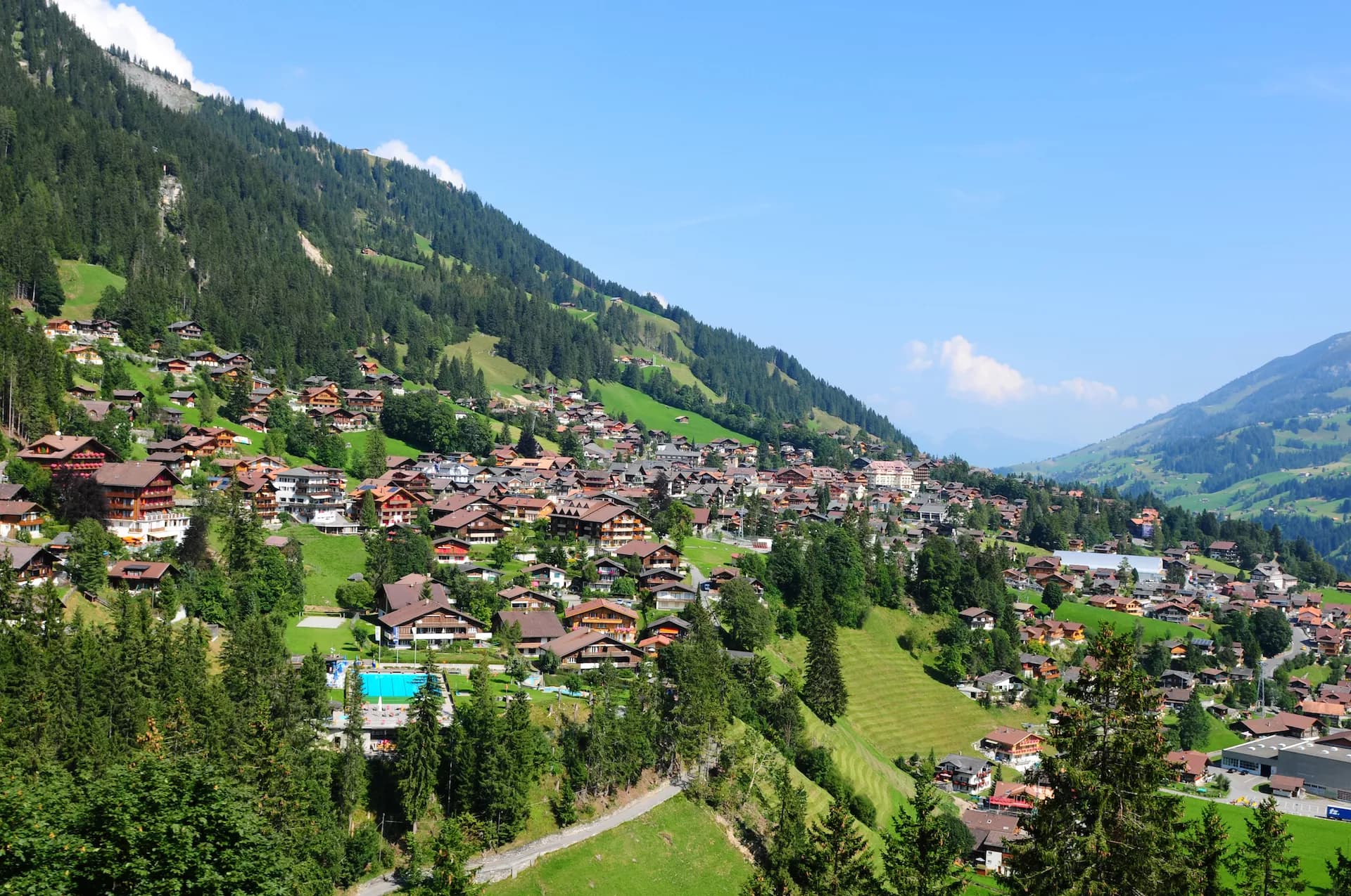 Alpine village of Adelboden in Bernese Oberland nestled on steep green slopes under a blue sky.