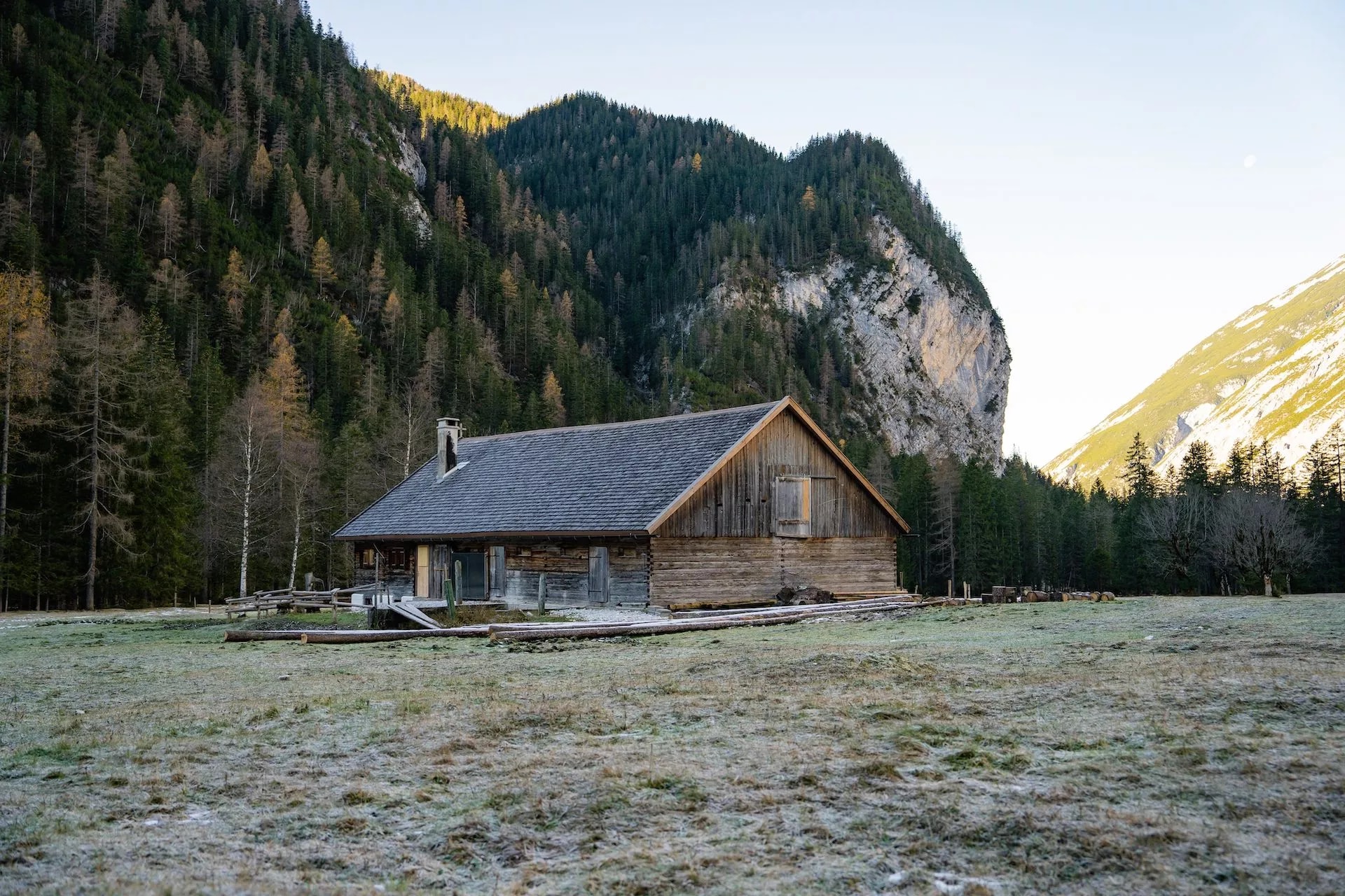 Wooden Kastenalm hut in a frosty meadow below steep, forested alpine mountains.