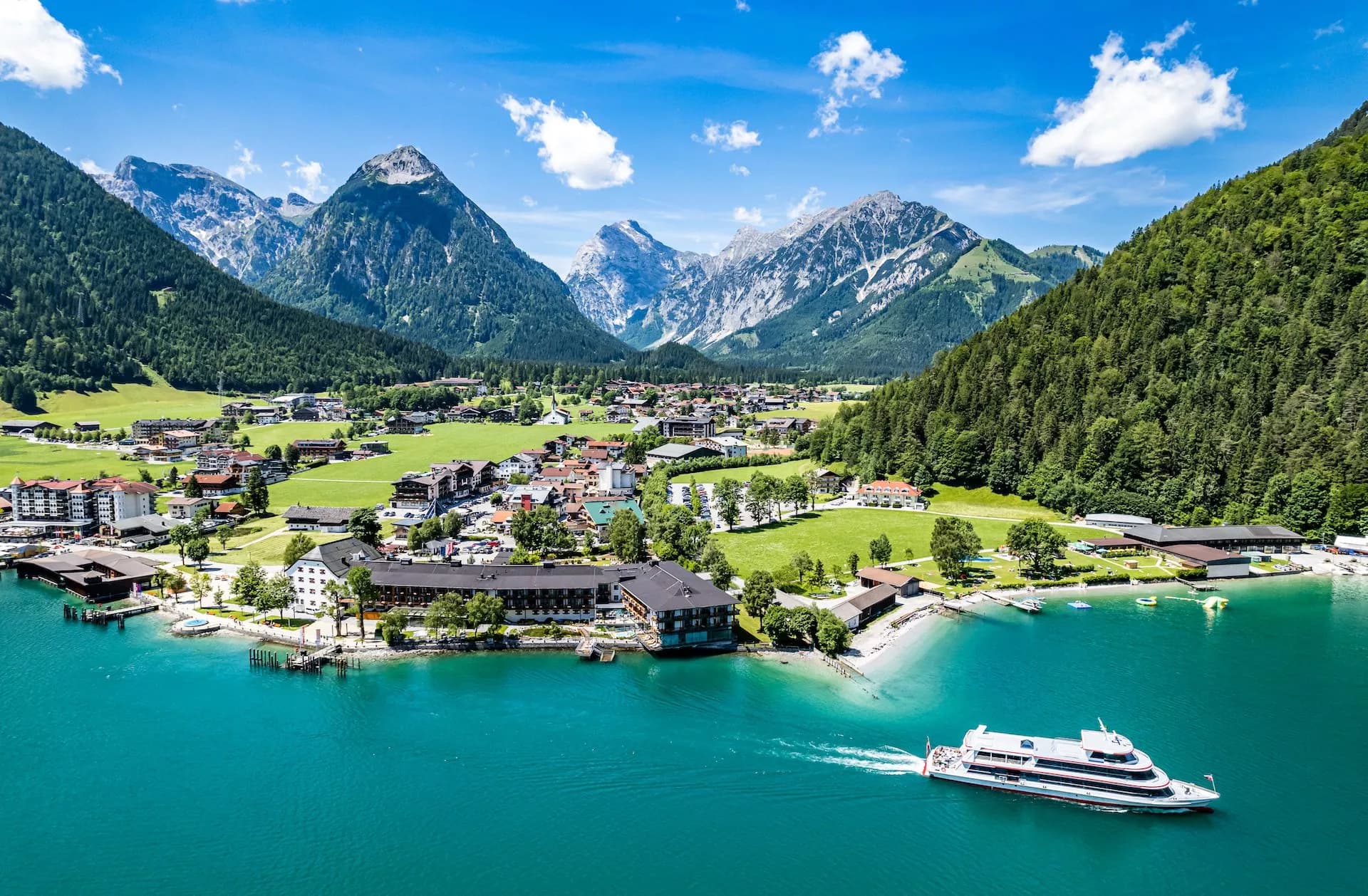 Ferry boat on turquoise alpine lake near village nestled in green mountains under blue sky