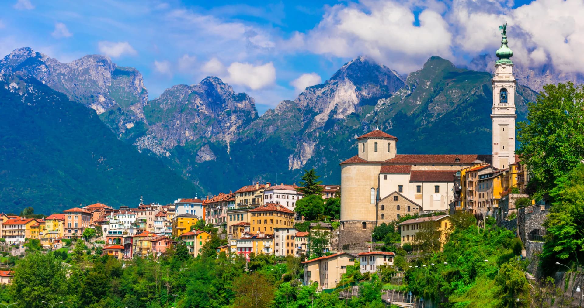Belluno town with colorful buildings and church tower set against dramatic, green Dolomite mountains.