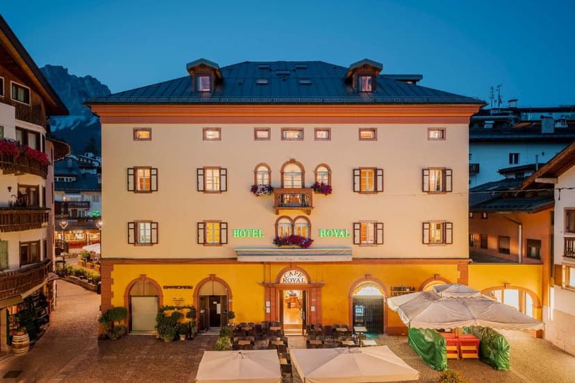Hotel Royal building facade with illuminated signs and outdoor cafe seating at dusk in an alpine village.