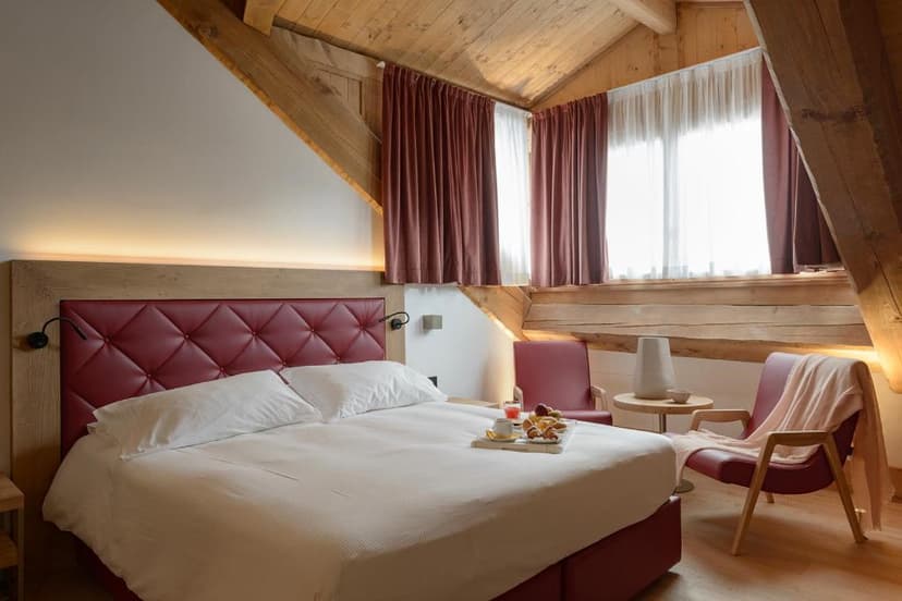 Hotel room with wood beams, white bedding, and a red tufted headboard, Royal Hotel Cortina.