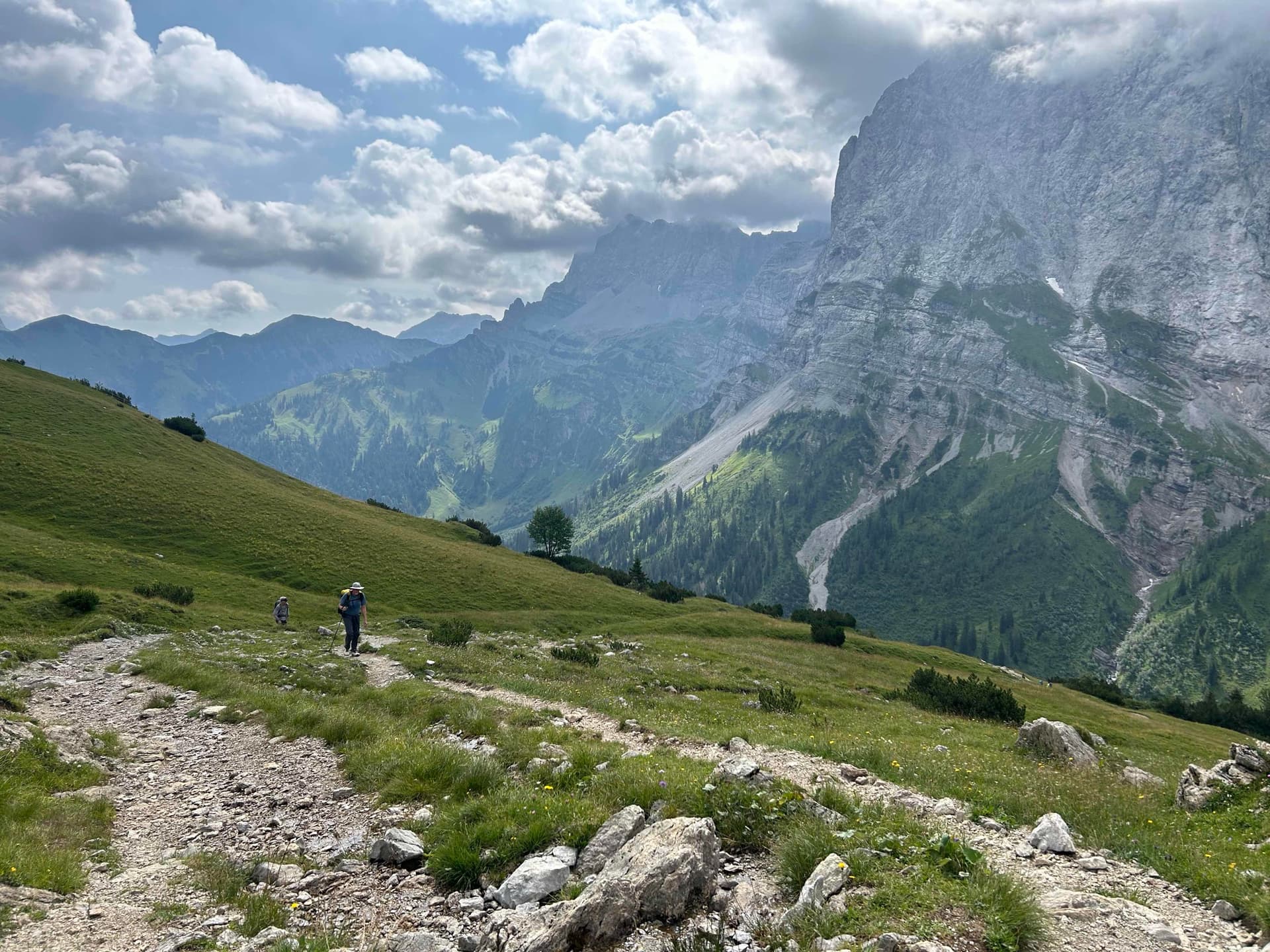 Hikers on rocky trail below towering cliffs and alpine mountains
