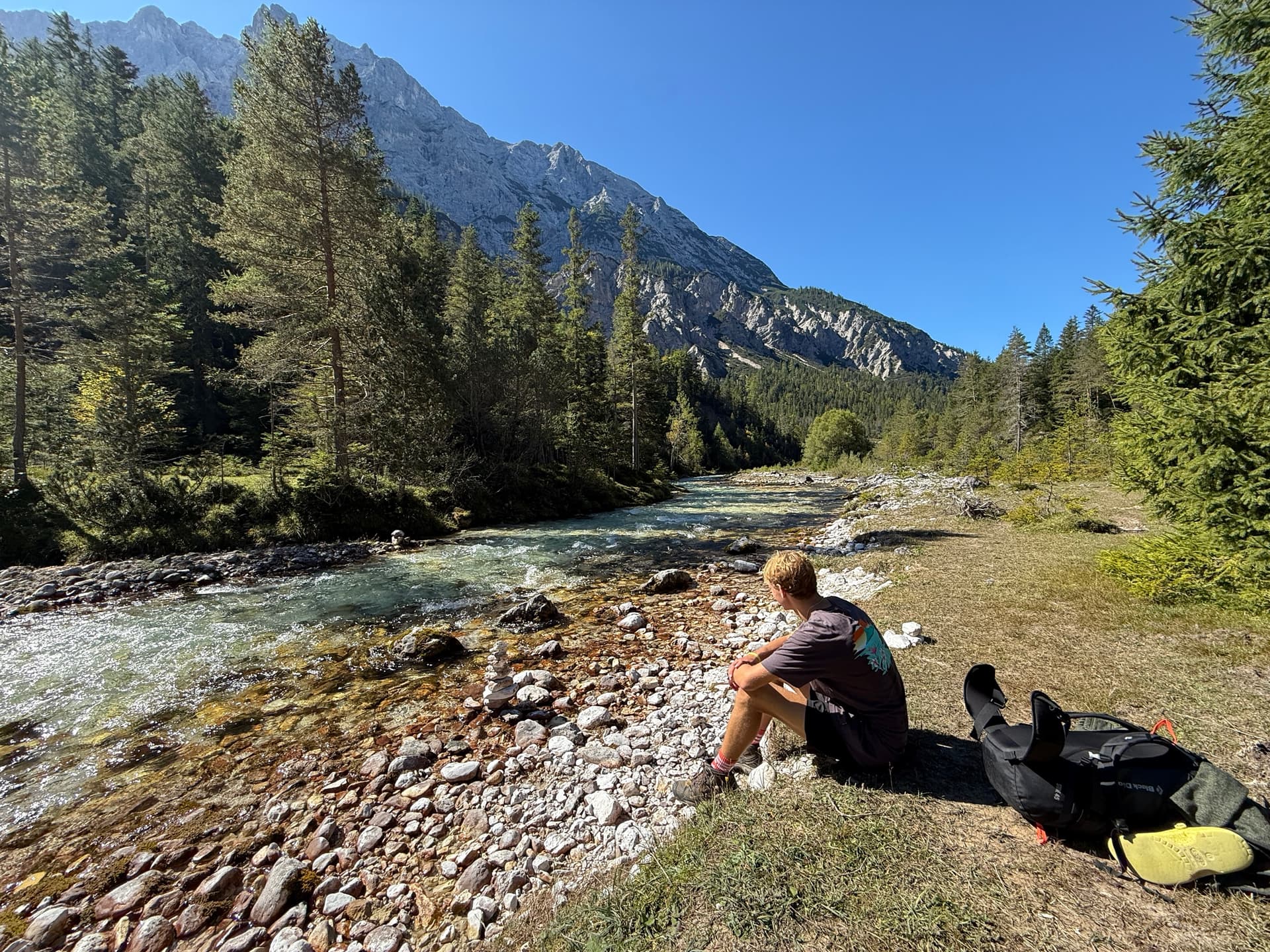 Hiker resting by rocky mountain river with backpack and pine trees
