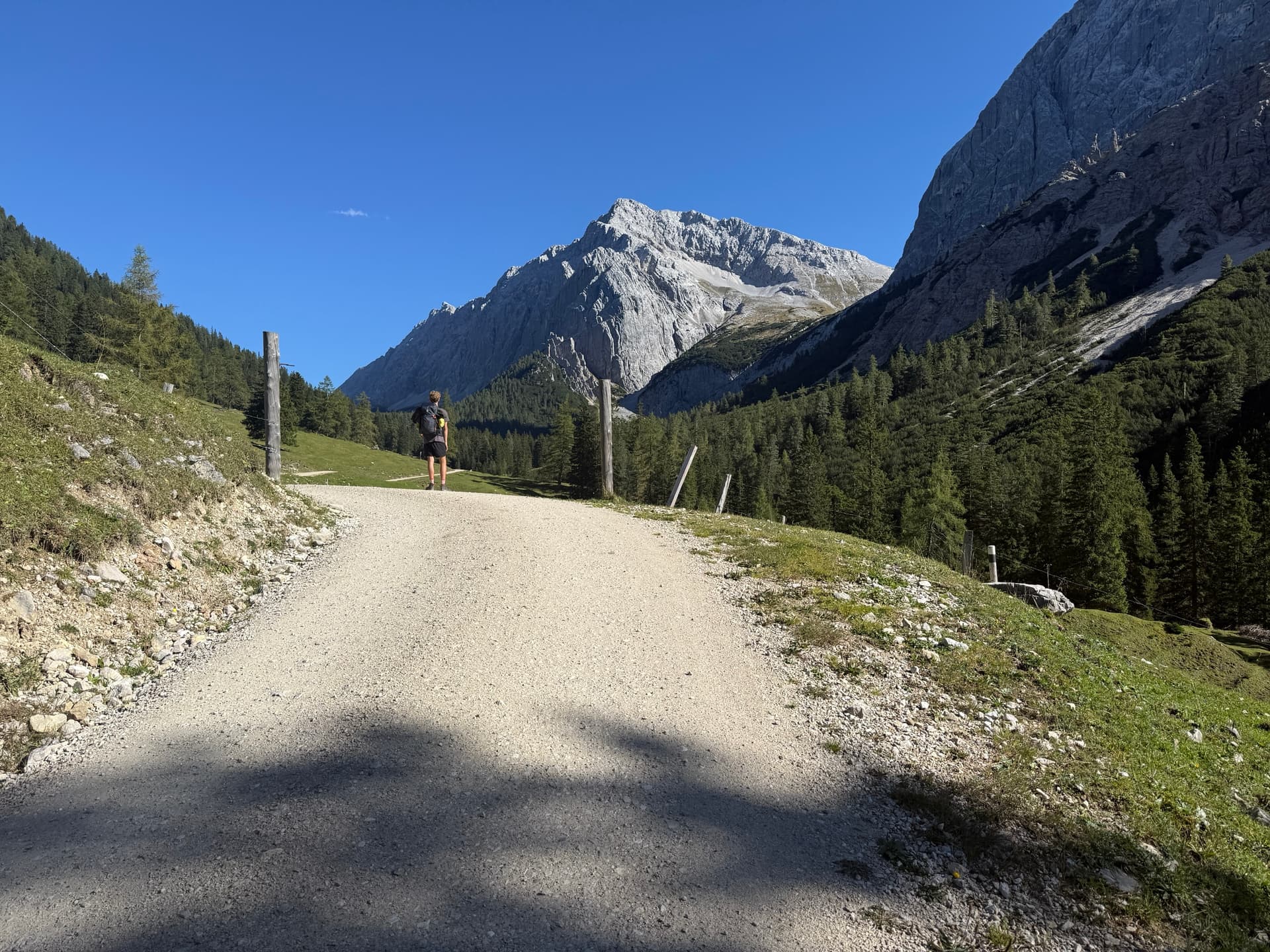 Hiker on gravel track through sunny alpine valley with rocky mountains