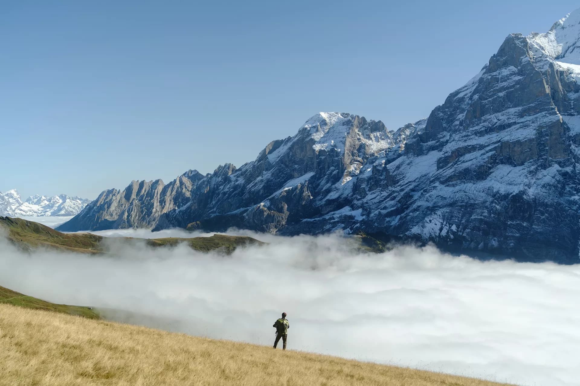 Hiker above cloud inversion viewing the snow-capped Eiger North Face from meadows above Grindelwald.